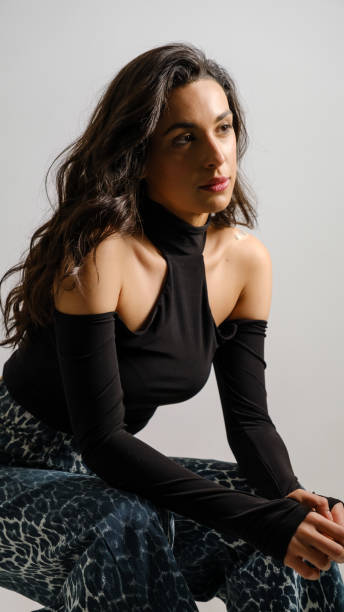 istock In a studio setting with a white background, a young black-haired woman wearing a black blouse and jeans strikes an artistic pose 2188278688