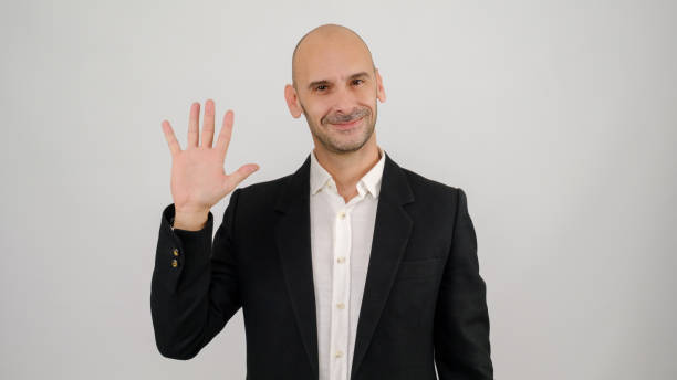 istock In a studio setting, a middle-aged businessman wearing a suit is standing in front of a white background, waving his hand and looking at the camera 2188279358