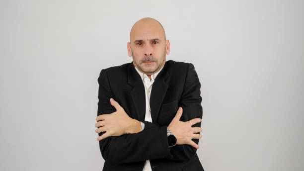 istock In a studio setting, a middle-aged businessman wearing a suit is standing in front of a white background, looking at the camera with an expression that shows he is cold 2188280068