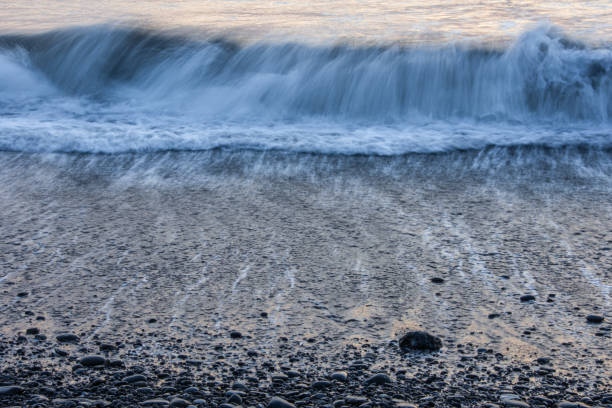 istock A long exposure of waves and foam on a beach with black pebbles. 2188280295