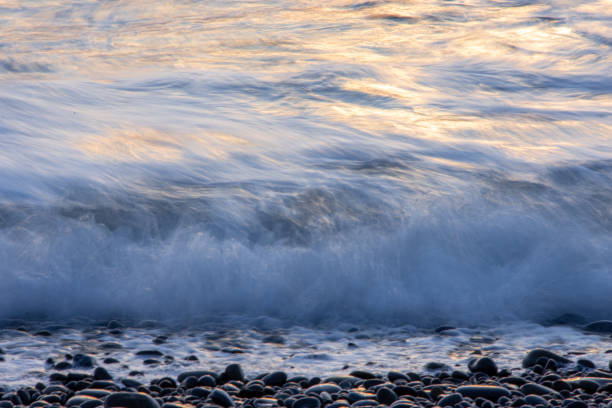 istock A long exposure of waves and foam on a beach with black pebbles. 2188280303