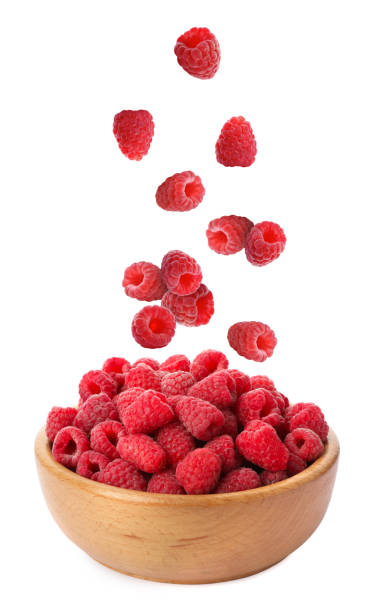 Fresh ripe raspberries falling into bowl on white background