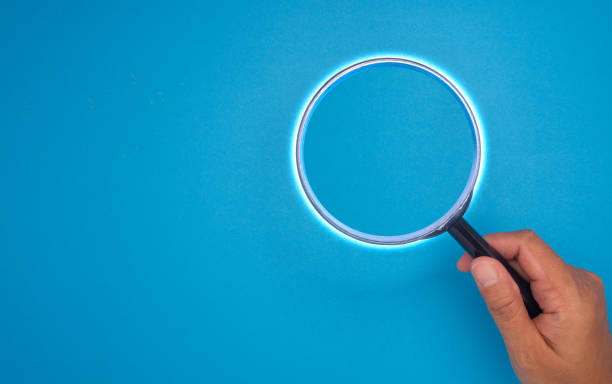 istock Hand holding a magnifying glass against a blue background. Top view. 2188307102