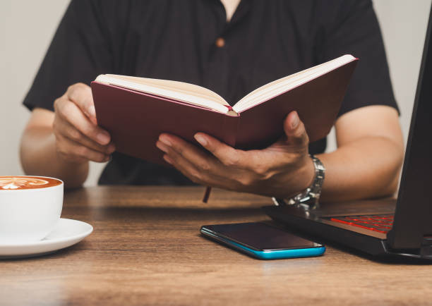 istock Close-up of a man holding an open book while seated at a desk. 2188307155