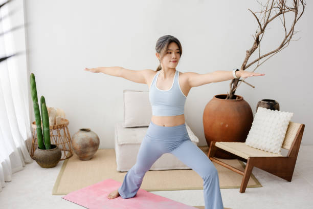A portrait of a beautiful Asian female yoga instructor focusing on stretching, strength, balance, and relaxation in a living room.