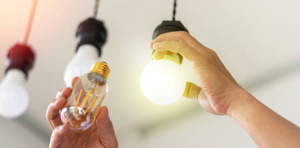 istock Power saving concept. Hands holding new Light Emitting Diode ( LED ) light bulb with light on and blur spiral compact-fluorescent (CFL) bulbs behind for copyspace. 2188314270