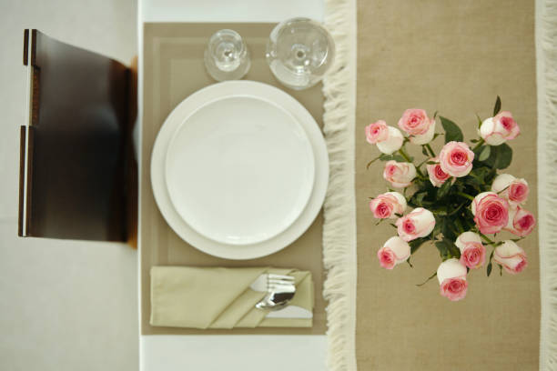 An outdoor dining table is artfully arranged for a gathering, featuring white chairs and a centerpiece of vibrant orange roses wrapped in paper, complemented by matching plates.
