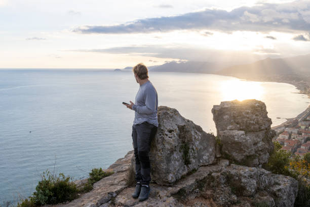 istock Young man uses mobile phone above sea at sunset 2188325443