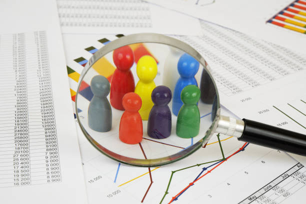 Management, demography and statistics concept. Different colored wooden people figures under magnifying glass on financial report.