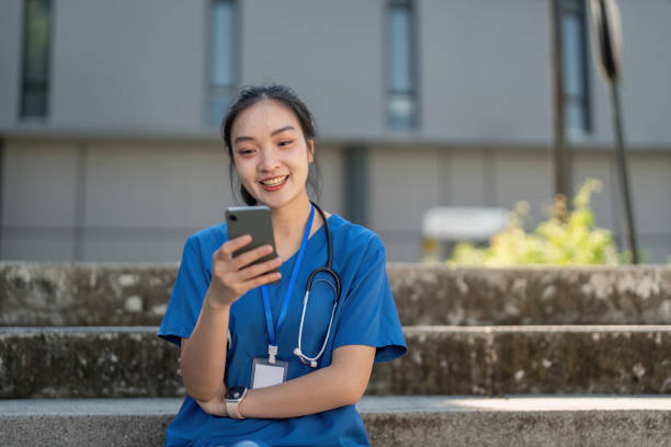 istock Asian nurse sitting on stairs using smartphone 2188336393