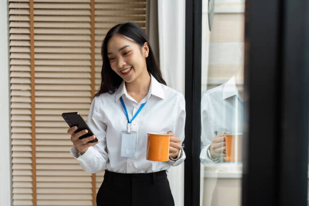 istock Professional Woman Smiling While Using Smartphone and Holding Coffee Cup in Modern Office Setting 2188338887