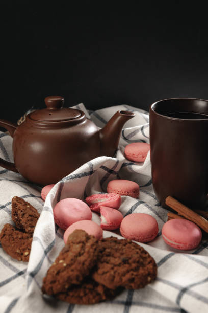 Teapot and cup on kitchen cloth with scattered pink macarons, close up