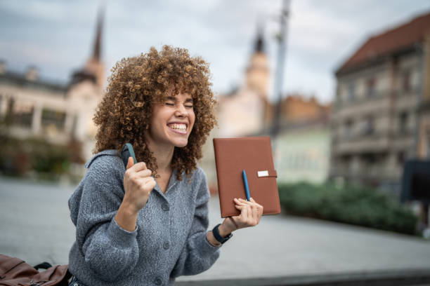 A young female student beams with excitement and pride after successfully passing her exam. With a sense of achievement, she celebrates her hard work paying off, feeling relieved and thrilled about her academic success. Her joyful expression reflects the satisfaction of reaching an important milestone in her studies.
