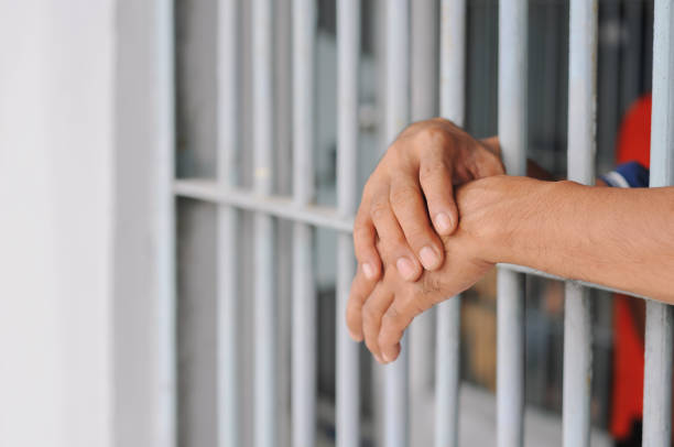 istock hands of a prisoner behind prison bars on black background 2188343948