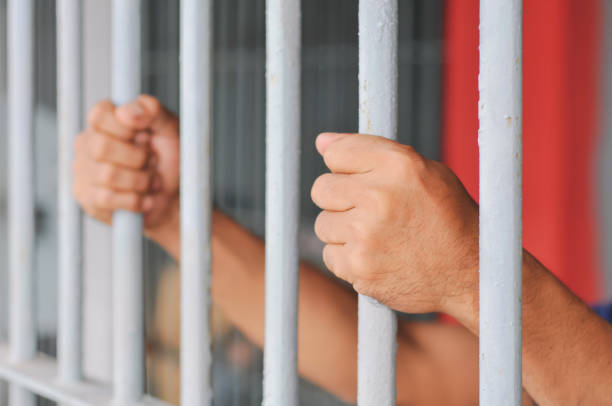 istock hands of a prisoner behind prison bars on black background 2188343955