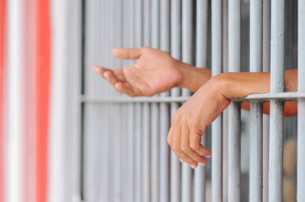 istock hands of a prisoner behind prison bars on black background 2188343975