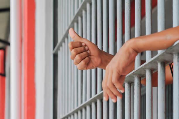 istock hands of a prisoner behind prison bars on black background 2188343995