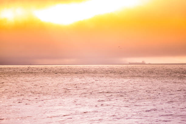 Ocean sunset scene with dramatic orange sky and distant ship on the horizon. Captures serene and tranquil atmosphere with reflections over calm sea, perfect for peaceful and soothing settings