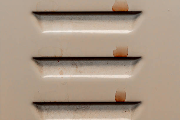 Rust stains are developing on a beige metal ventilation grill, highlighting the effects of corrosion and weathering