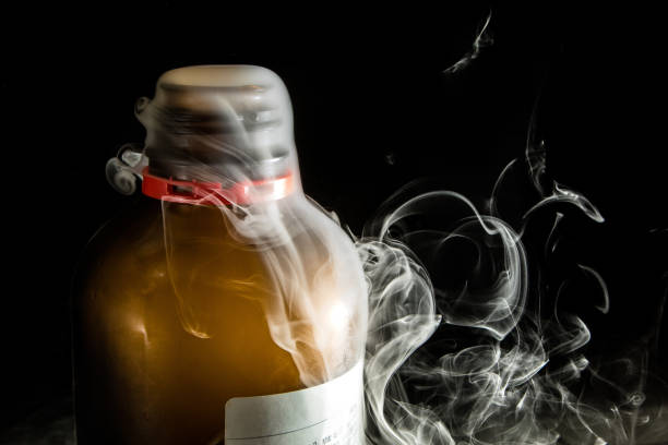White smoke is escaping from a brown reagent bottle with a red cap in a laboratory setting with a black background