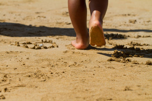 Close-up of small feet walking on a sandy beach, leaving footprints