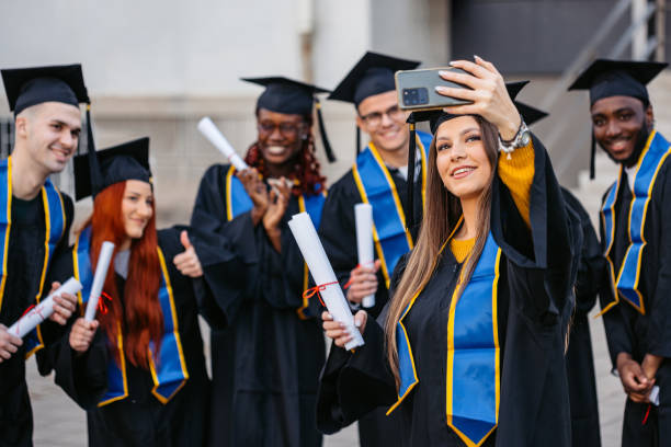 istock Students In Graduation Gowns Taking Selfies Using Phone On The University Campus 2188357307