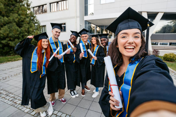 istock Students In Graduation Gowns Taking Selfies On The University Campus 2188357877