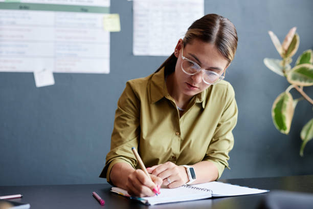 istock Woman Writing in Notebook during Test in Class while Studying English Language 2188359079