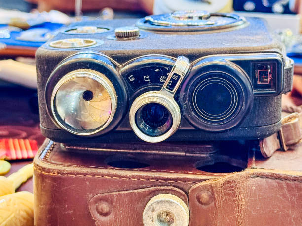 An old camera with a damaged lens and missing components on top of an antique suitcase.