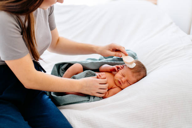 istock Mother gently brushes sleeping newborn on white bed 2188368996