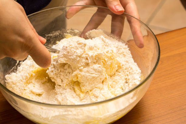 Hands mixing flour into dough with a fork in a glass bowl, preparing ingredients for baking
