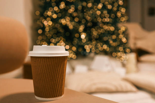 istock Takeaway coffee cup in eco-friendly brown paper holder with white lid, placed on a soft background with Christmas tree bokeh lights. Perfect for festive, cozy, and eco-conscious themes 2188371656