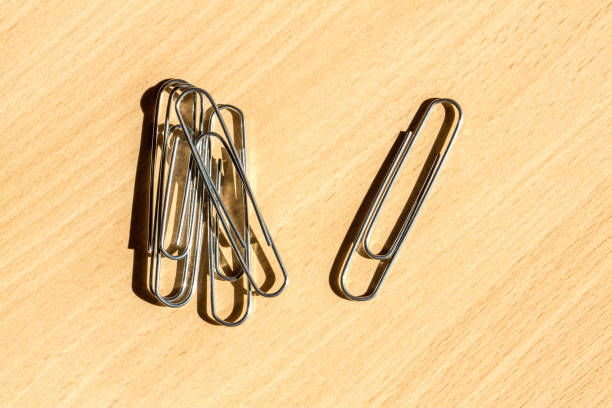 Metal paper clips on a wooden table in the sunlight are casting long shadows