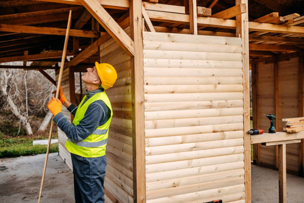 Mature man enjoying building a wooden house holding a plank and wearing safety equipment
