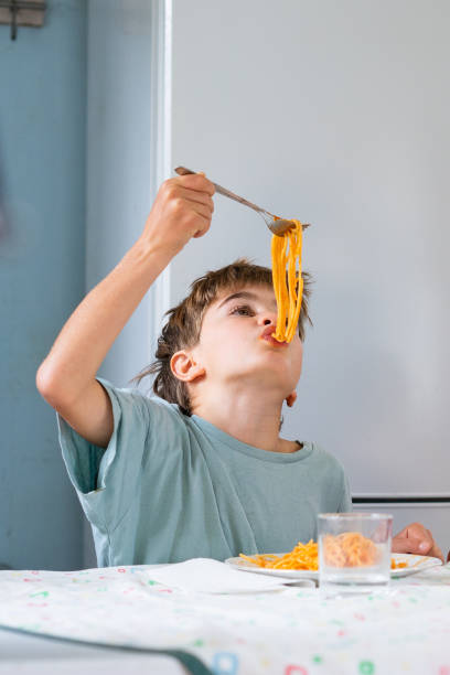istock Child enjoying spaghetti: lifting fork to mouth at kitchen table 2188379006