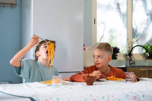 Children eating spaghetti with tomato sauce at home having fun