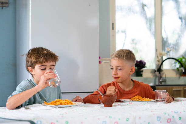 istock Two brothers eating spaghetti with tomato sauce and drinking water in the kitchen 2188379018