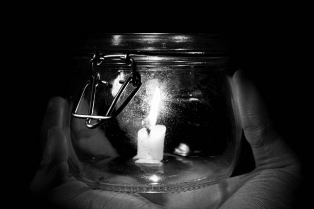 Hand holding a glass jar containing a lit candle