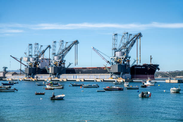 Lissabon, Lisboa - Portugal - 09-30-2024: Several small boats float on calm blue water in front of a harbor with large cranes and the cargo ship KYPROS SEA in the background.