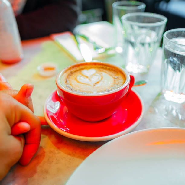 Enjoy a romantic coffee date with latte art in a cozy cafe. The image shows a red coffee cup and holding hands, capturing a perfect morning experience.