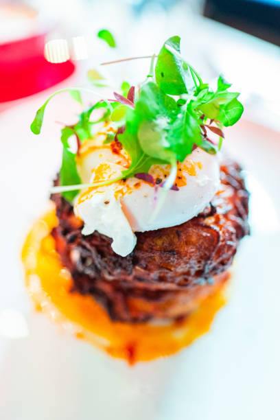 Delicious brunch dish with poached egg on crispy hash browns, garnished with fresh microgreens and vinaigrette, served on a white plate. Ideal for fine dining or gourmet culinary promotions.