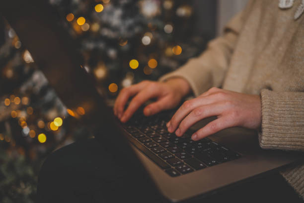 istock Hands typing on a laptop with a beautifully glowing Christmas tree in the background, creating a cozy and festive atmosphere indoors 2188383422