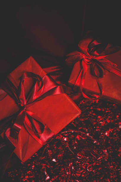 Moody and dramatic Christmas composition with red-wrapped gift boxes tied with shiny ribbons, surrounded by sparkling sequins and festive elements in low light.