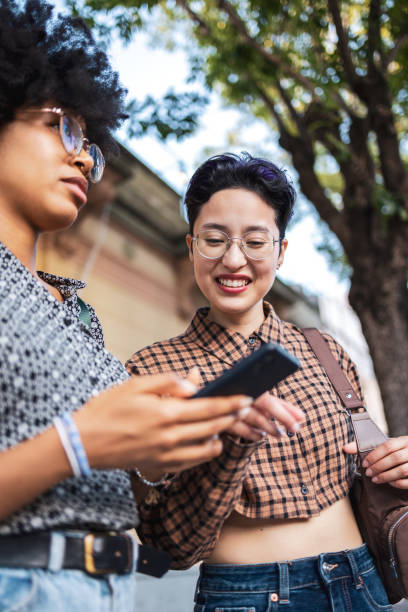 istock Two friends sharing a laugh while engaging with a mobile device outdoors 2188387736
