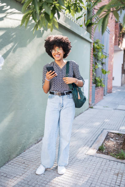 istock Smiling woman using smartphone on a sunny street with green foliage 2188389321