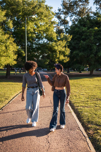 istock Two friends walking and chatting in a sunny park setting 2188389344