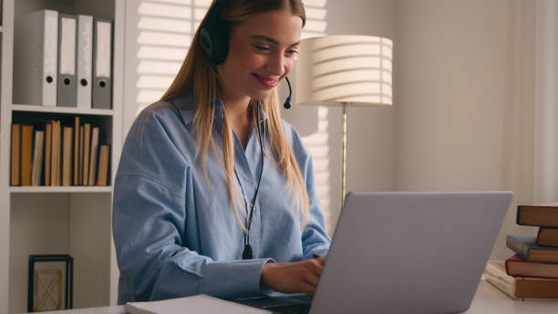 istock Caucasian woman in headset conference calling on laptop online teacher studying e-learning from home library with books writing notes write homework student girl learning computer distance education 2188391916