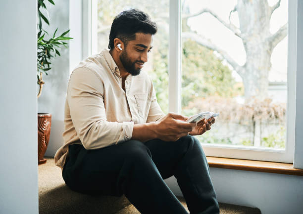 istock Young Man Sitting on Stairs Using Smartphone with Wireless Earphones 2188392598