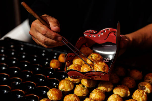 A vendor skillfully serves Japanese Takoyaki using chopsticks