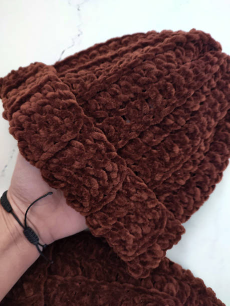 istock Knitted hat in hand, dark brown chocolate beanie hats on white marble background top view flat lay, velor, velvet hat, crochet, pair, set, autumn winter headwear, warm cosy accessory, yarn, pattern 2188401464